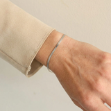 Silver snake bracelet on a wrist with a neutral background