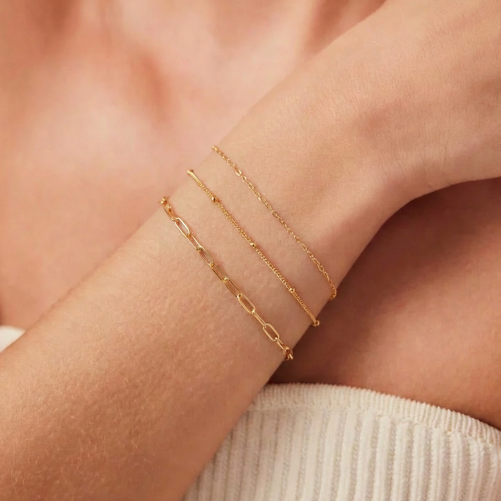 Gold bracelets on a person's wrist with a neutral background. Permanent bracelet.