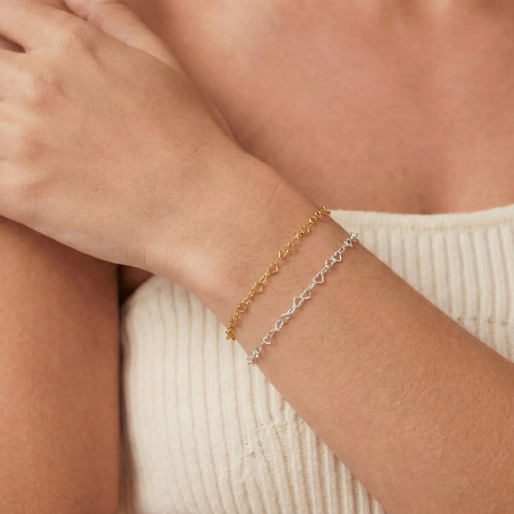 Close-up of a person's wrist wearing two gold bracelets on a neutral background. Permanent jewelry bracelets.